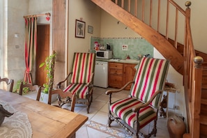 Un coin repas avec des chaises et une table en bois, une cuisine équipée d’un four à micro-ondes et d’une cuisinière, et un escalier avec des rampes en bois.