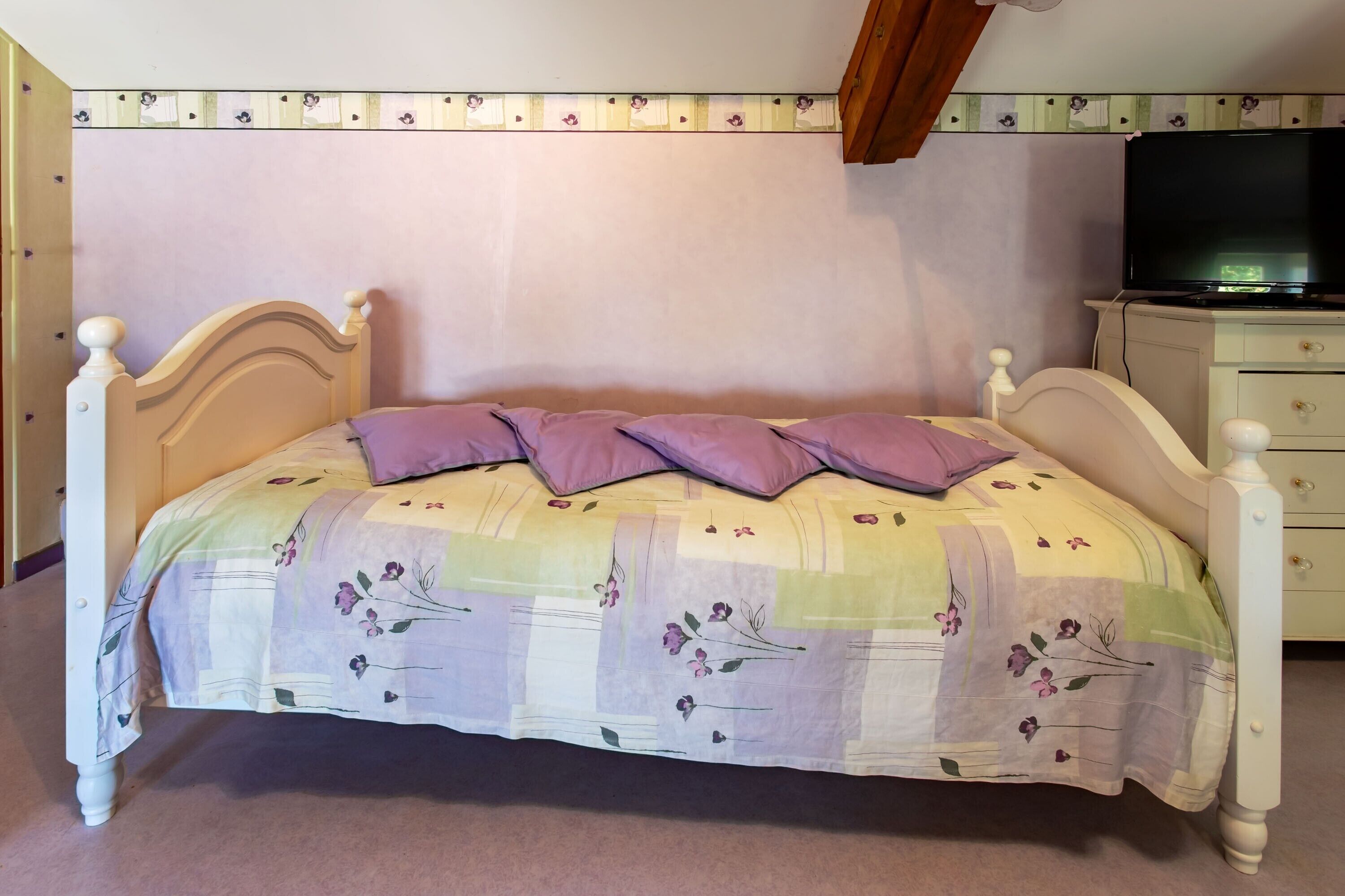 A bed with a floral bedspread, a television on a stand, and a dresser with drawers.
