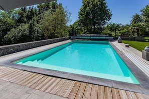Une piscine rectangulaire entourée d’une terrasse en bois, avec un paysage arboré en arrière-plan.