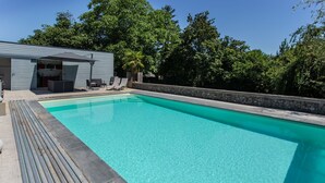Una piscina rectangular de aguas cristalinas, rodeada por un muro de piedra y una terraza de madera.