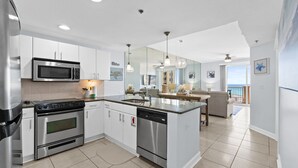 A modern kitchen with stainless steel appliances, a central island, and a view to a balcony. - Grand Panama PCB 2BR Beach Views 2 Pools Sleeps 8 (Panama City Beach)