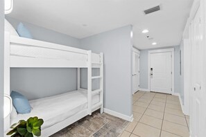 A room with bunk beds, a small plant, and a door leading to another room. - Grand Panama PCB 2BR Beach Views 2 Pools Sleeps 8 (Panama City Beach)