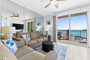 A modern living room with a sofa, ottoman, and a large window with a view of the ocean. - Grand Panama PCB 2BR Beach Views 2 Pools Sleeps 8 (Panama City Beach)