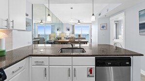 A modern kitchen with a granite countertop, stainless steel appliances, and a fire extinguisher sign. - Grand Panama PCB 2BR Beach Views 2 Pools Sleeps 8 (Panama City Beach)