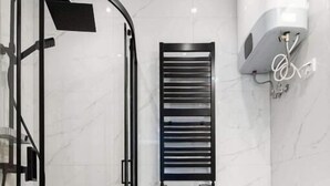 A modern bathroom with a glass-enclosed shower, a built-in toilet, a washing machine, and a towel rack. - Malila Apartaments Cracow Center Dunin 3 (Kraków)