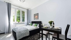 A modern bedroom with a bed, a dining table, and a window with curtains. - Malila Apartaments Cracow Center Dunin 3 (Kraków)