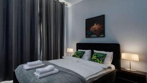 A hotel room with a bed, two bedside lamps, a painting on the wall, and a window with curtains. - Malila Apartaments Cracow Center Dunin 3 (Kraków)