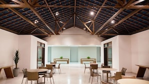 Une pièce spacieuse avec un plafond haut, de nombreuses tables et chaises, et une grande fenêtre au fond.