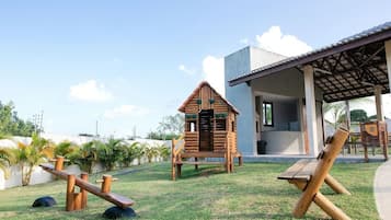Un parque infantil con estructuras de juego de madera, una zona de estar cubierta y un edificio de diseño moderno.