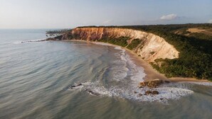 Un paysage côtier caractérisé par une plage en forme de courbe, des falaises et une végétation luxuriante.