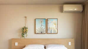 Une chambre à coucher avec une tête de lit en bois, deux oreillers blancs, une couverture matelassée marron et deux tableaux représentant des motifs floraux, encadrés et accrochés au mur.