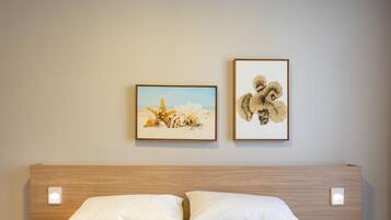 A bed with a quilted brown cover, two white pillows, and a wooden headboard. Two framed artworks are hung on the wall above the bed.