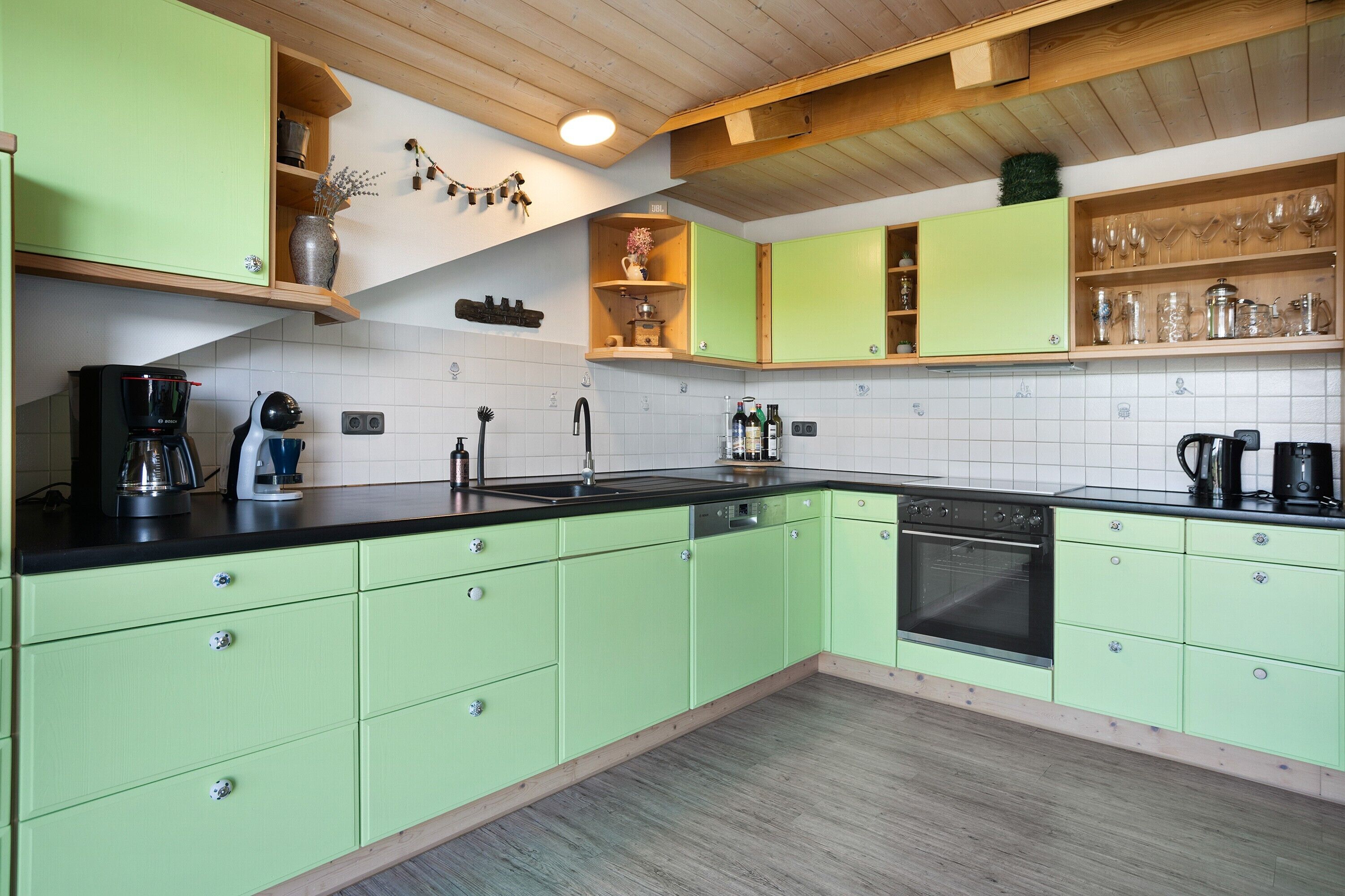A kitchen with green cabinets, a black sink, and a wooden ceiling.