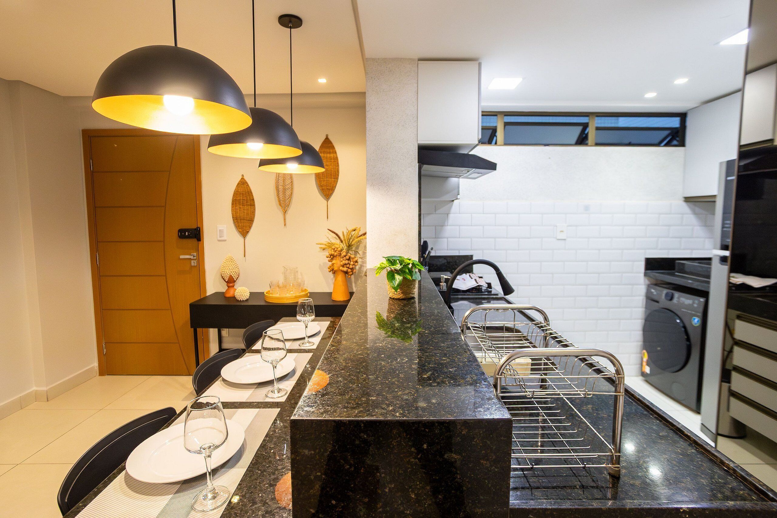 Uma cozinha moderna com bancada de mármore preto, forno embutido e máquina de lavar.