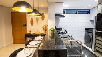 Uma cozinha moderna com bancada de mármore preto, forno embutido e máquina de lavar.