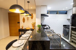 A modern kitchen with a black marble countertop, a built-in oven, and a washing machine. - Enseada de Coqueirinho #201 - Apt by Carpediem (João Pessoa)