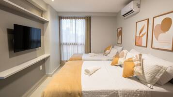 Quarto de hotel com duas camas, televisão de tela plana, ar condicionado e obras de arte nas paredes.