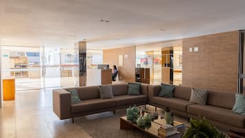 Um lobby moderno com sofá em formato de L, mesa de centro com objetos decorativos e divisória de vidro.