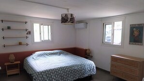 A bedroom with a bed, a dresser, a shelf with decorative items, and a window. - Modern Creole house with swimming pool, garden and sea view (Etang Salé les Hauts) (L'Étang-Salé)
