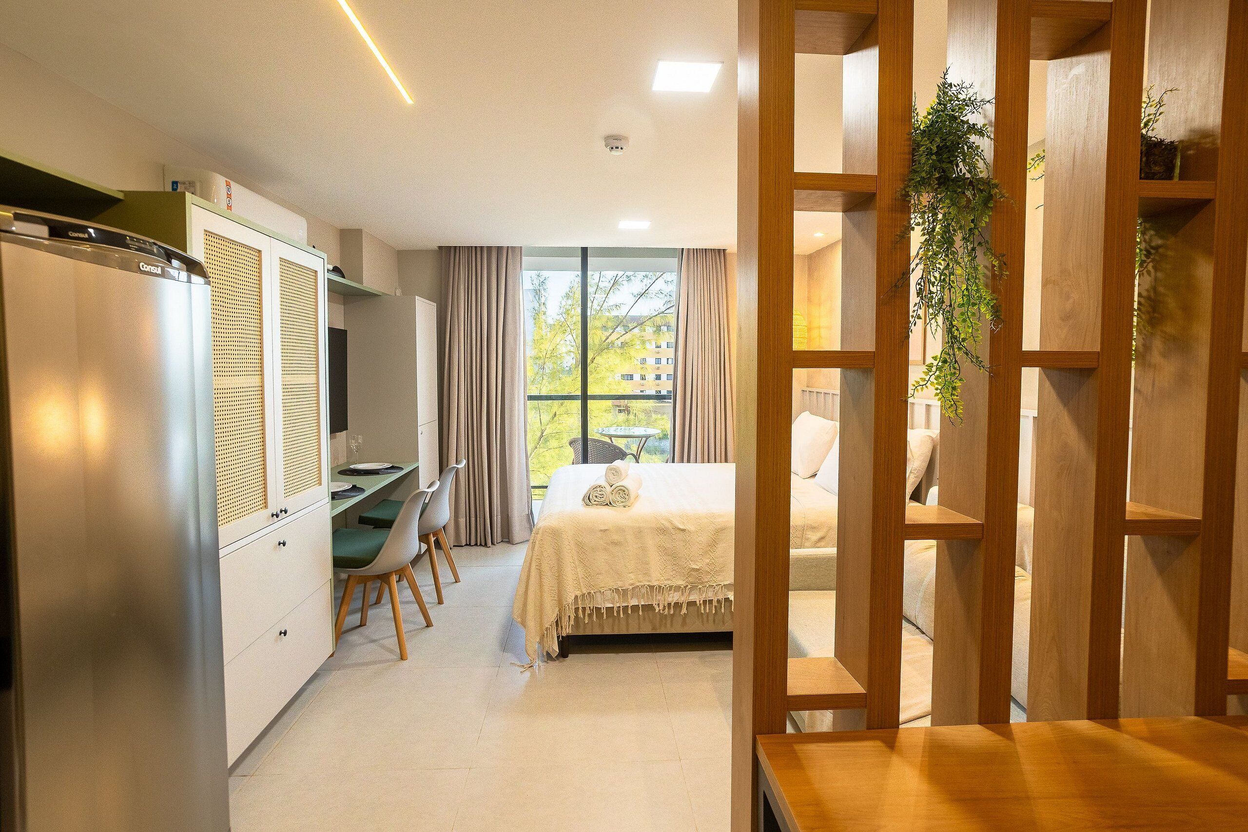 Quarto de hotel pequeno com uma cama, uma escrivaninha e uma cozinha compacta.