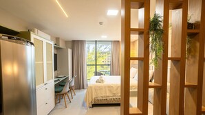Ett kompakt hotellrum med en säng, ett skrivbord och ett litet kök.