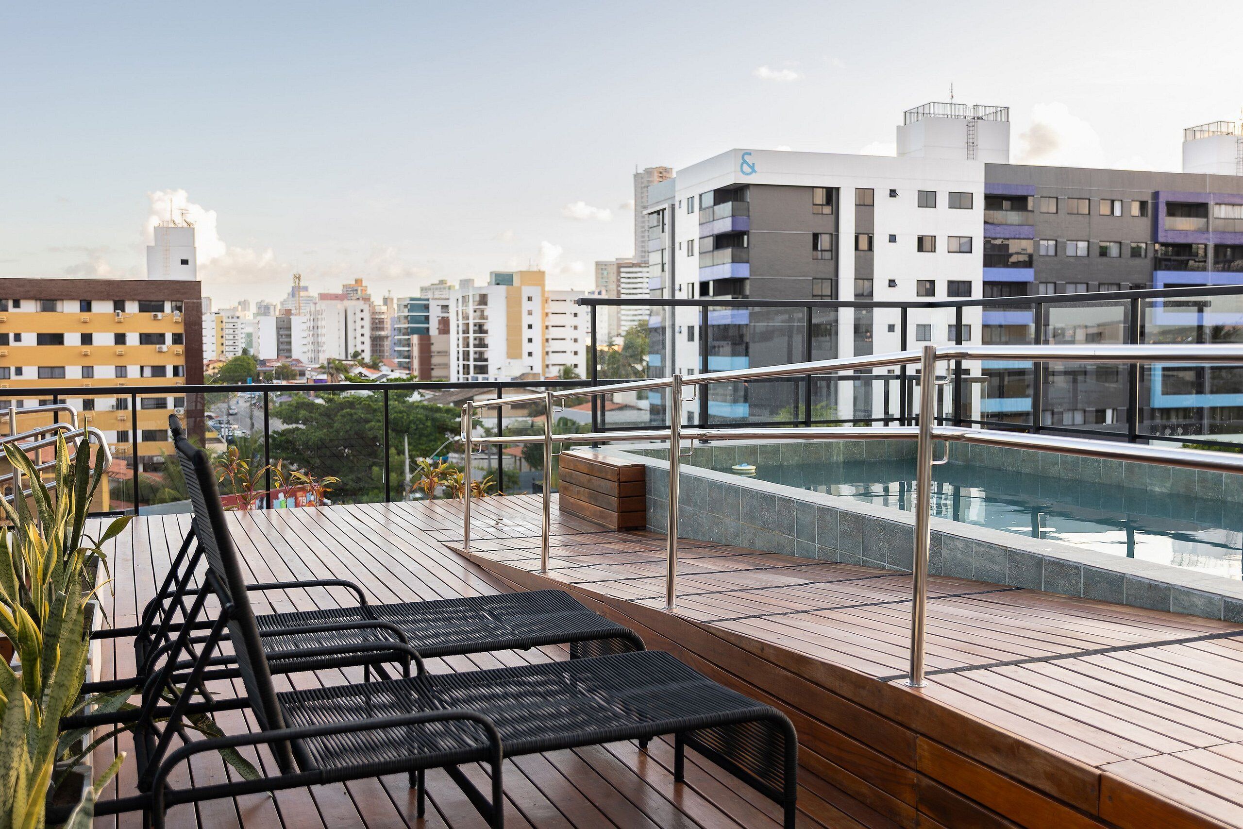 Terraço no telhado com piscina, deck de madeira e espreguiçadeiras pretas.
