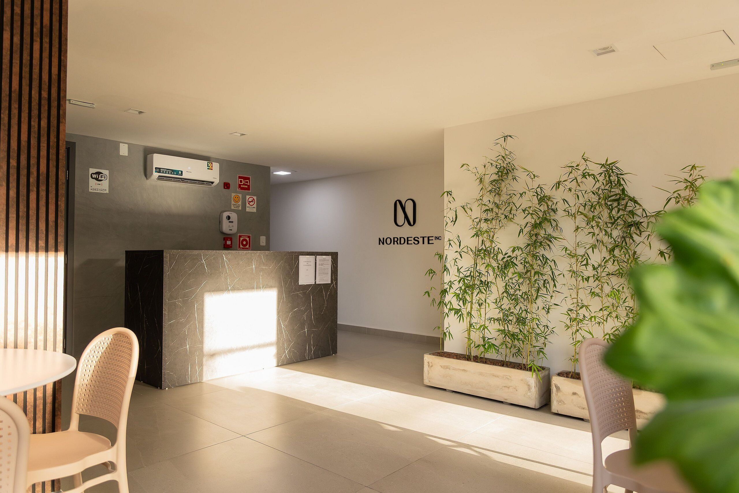 Uma área de recepção com um balcão de mármore, uma grande planta de bambu em vaso e uma placa com a inscrição Nordeste Inc.