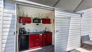 Une cuisine de taille réduite avec des meubles rouges, un réfrigérateur noir et un four à micro-ondes.