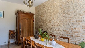 Une table à manger en bois avec des chaises, un chemin de table en dentelle, un buffet en bois et un mur en pierre.