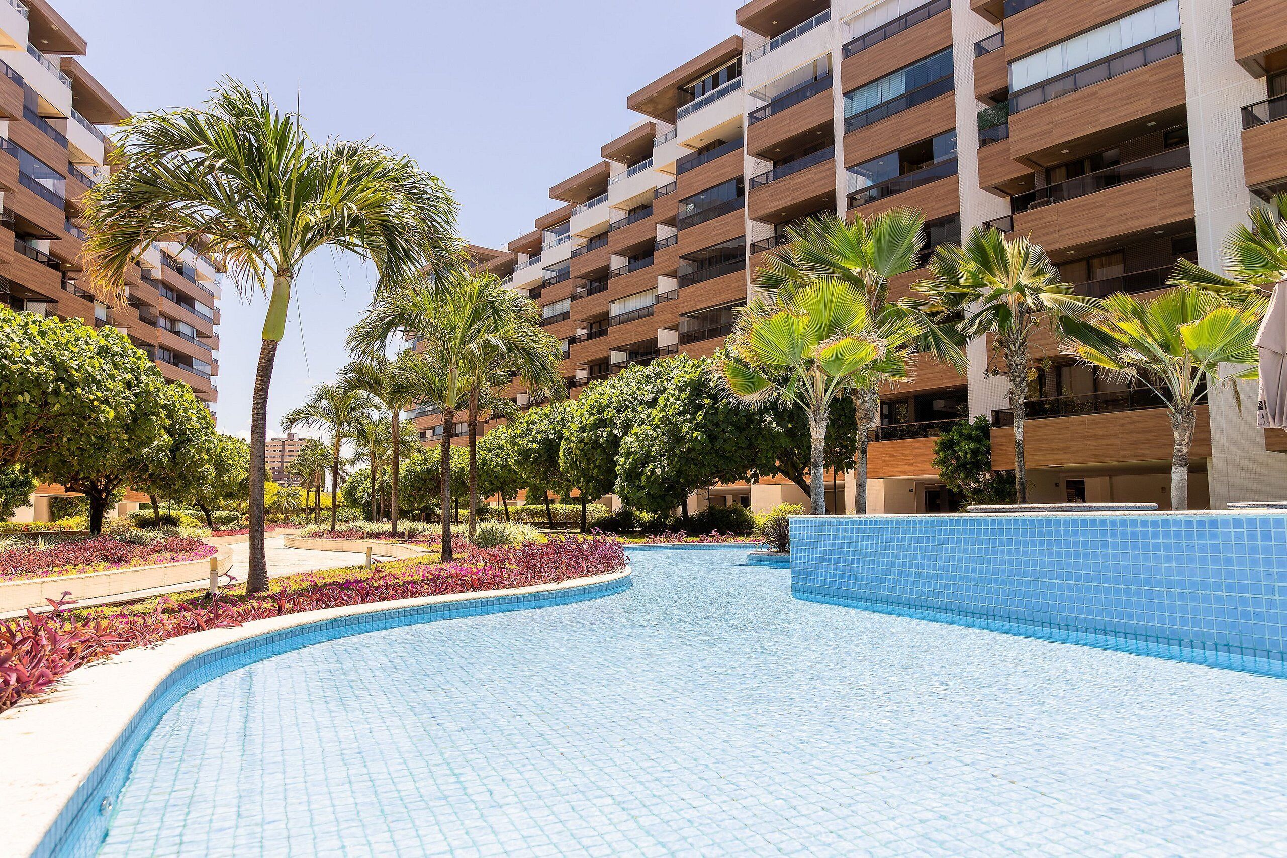 Un hôtel moderne doté d’une piscine, entouré de palmiers et d’un jardin aménagé.