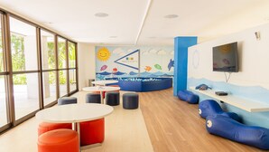 Ein Kinderspielbereich mit einer Meer-Mural, runden Tischen und bunten Sitzgelegenheiten.