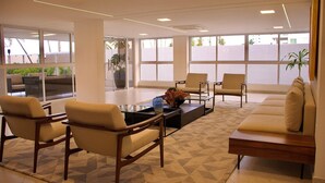 A modern waiting area with comfortable seating, large windows, and a geometric patterned floor. - Puerto Ventura #203 - Ape Ao Mar por Carpediem (João Pessoa)