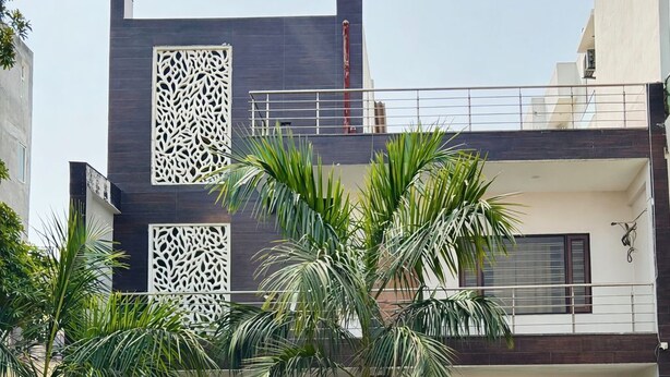 A modern two-story building with a balcony, a decorative wall, and a well-maintained lawn with palm trees. - The Prime Regency (Greater Noida)