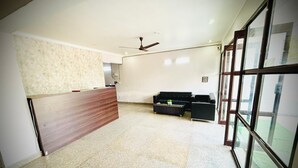 A spacious room with a reception desk, a ceiling fan, and large windows offering a view of the outdoors. - The Prime Regency (Greater Noida)