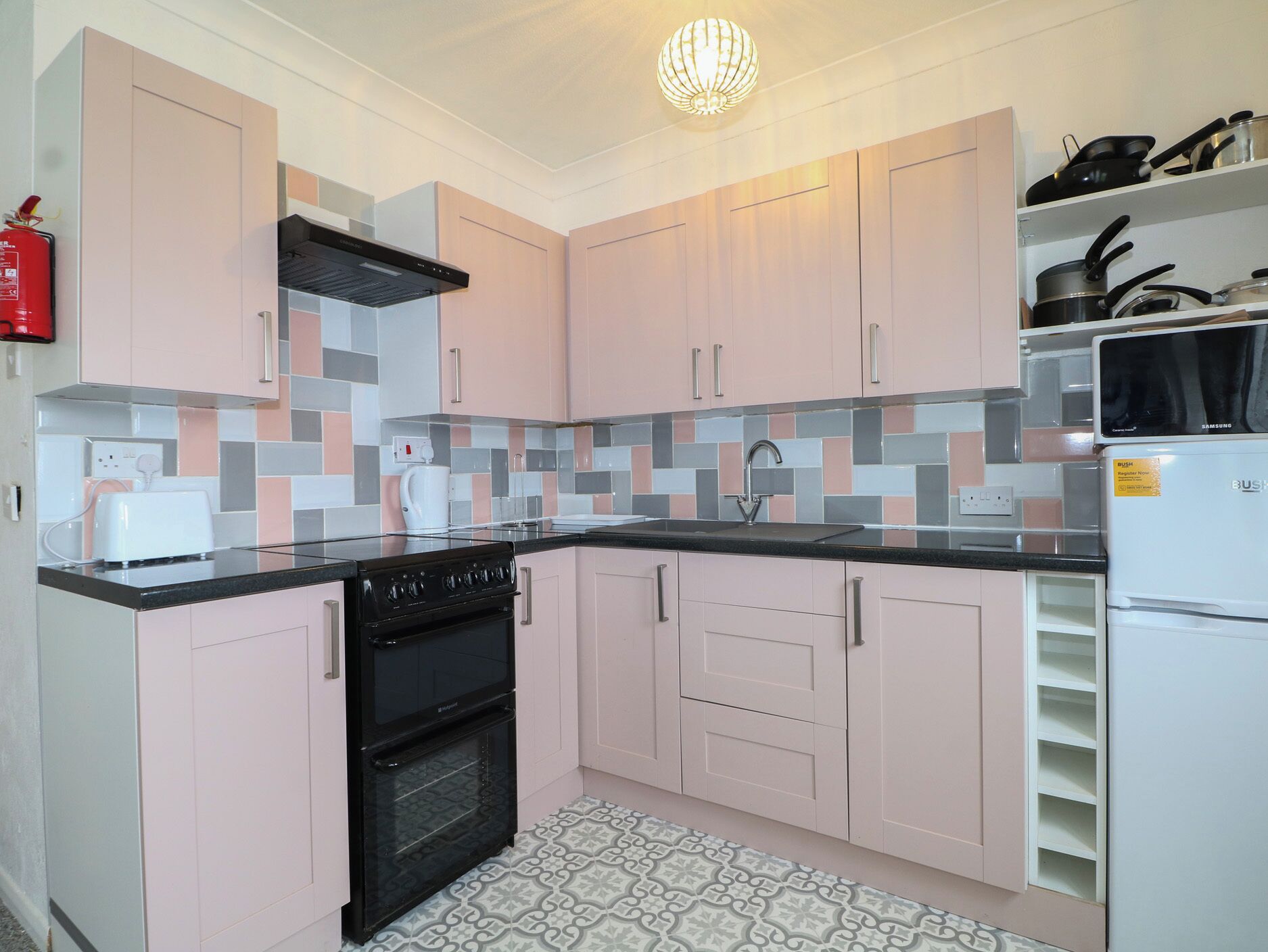 A modern kitchen with pink cabinets, a black stove, a sink, and a Samsung refrigerator.