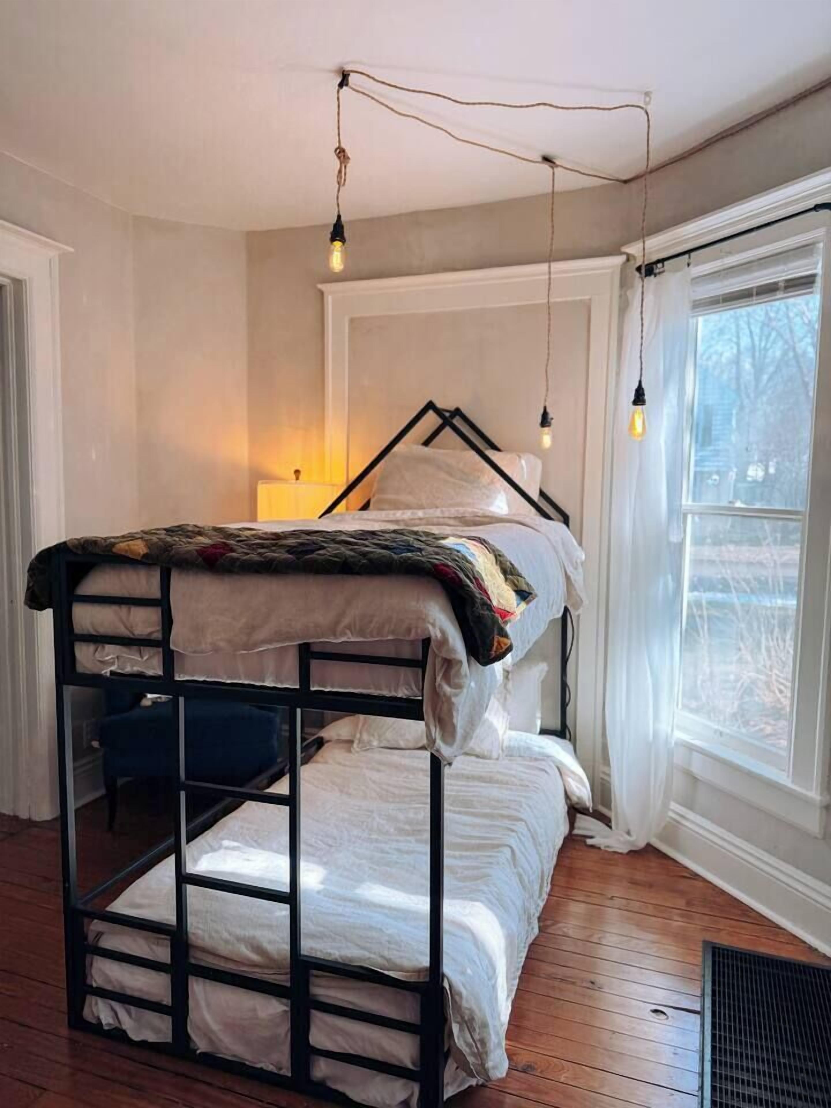 A bunk bed with a white headboard, a wooden floor, and a window with a view of trees.
