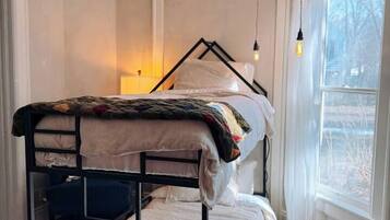 A bunk bed with a white headboard, a wooden floor, and a window with a view of trees.