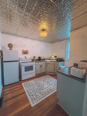 Una cocina con armarios blancos, una estufa, un refrigerador y una alfombra estampada.