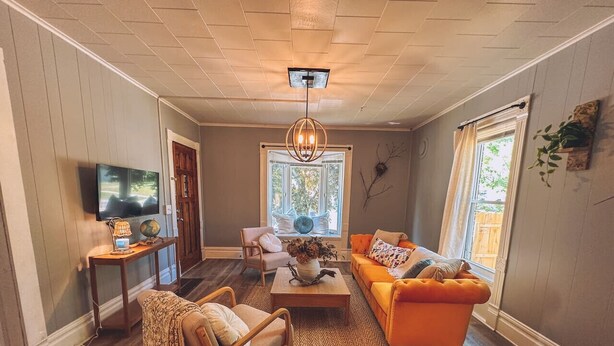 A living room with a wooden floor, a sofa, a chair, a coffee table, a TV, and a window with curtains. - The Row House on 4th (Dowagiac)