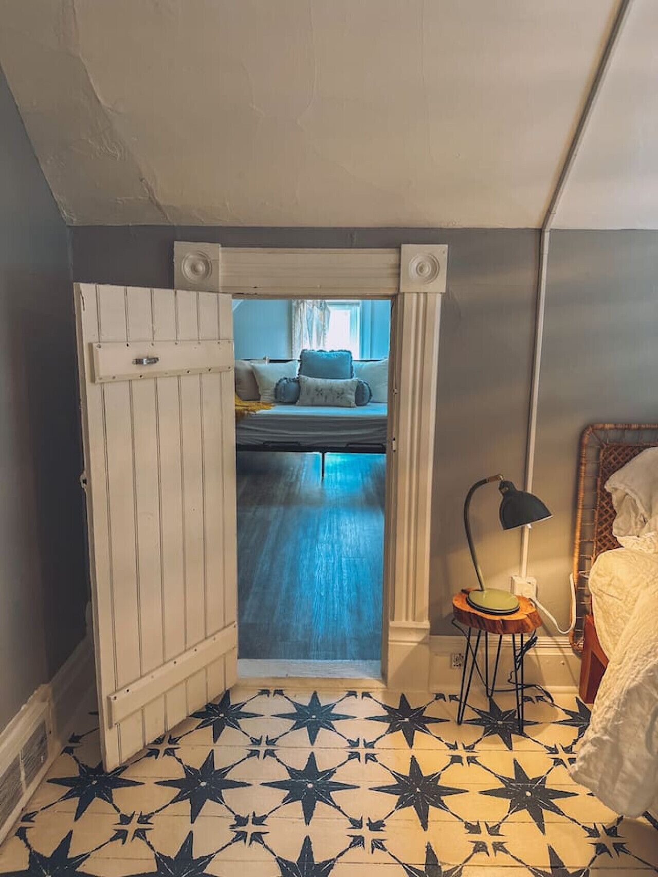 A room with a bed, a small table with a lamp, and a star-patterned floor.