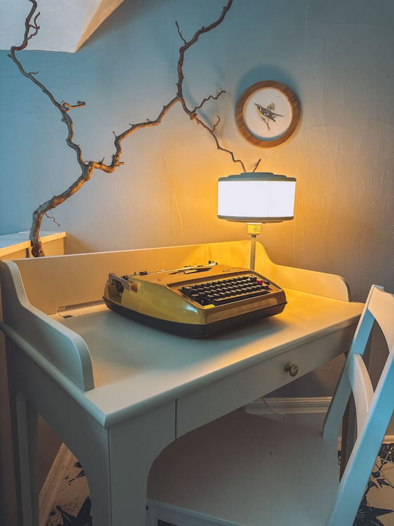 A desk with a typewriter, a lamp, and a wall clock.