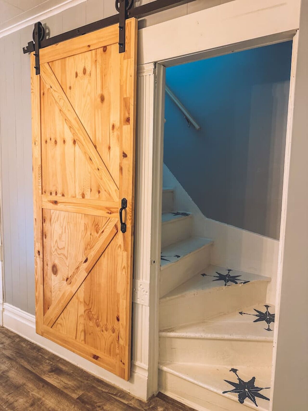 A wooden barn-style sliding door with a black metal track, leading to a staircase with white walls and star-shaped decorations on the steps.