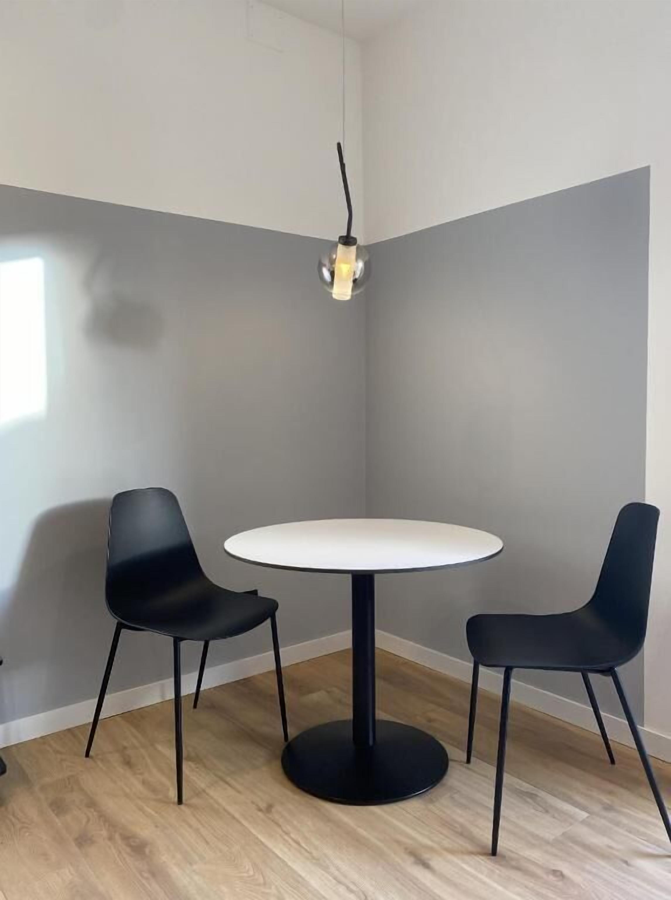 Ein Zimmer mit einem runden Tisch, zwei schwarzen Stühlen, einer Hängelampe und Holzboden.