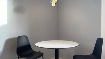 Ein Zimmer mit einem runden Tisch, zwei schwarzen Stühlen, einer Hängelampe und Holzboden.