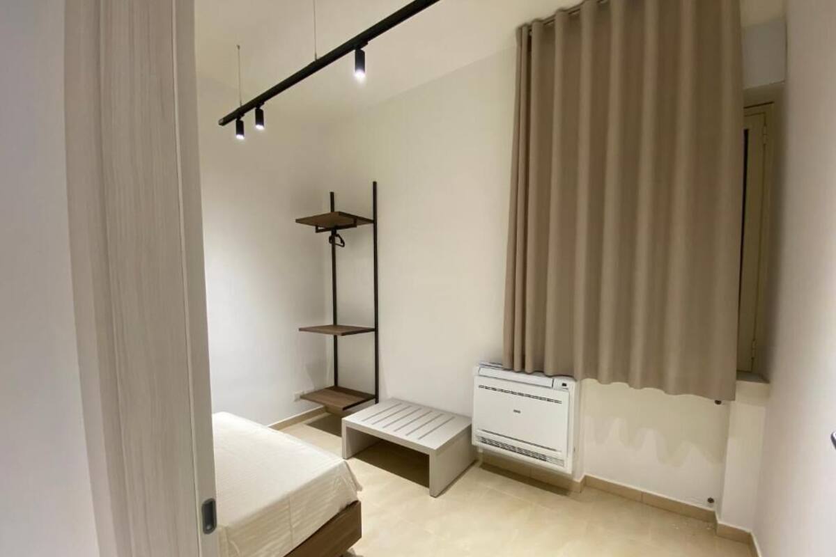 Une chambre à coucher comprenant un lit, un petit banc, une étagère et un radiateur fixé au mur.