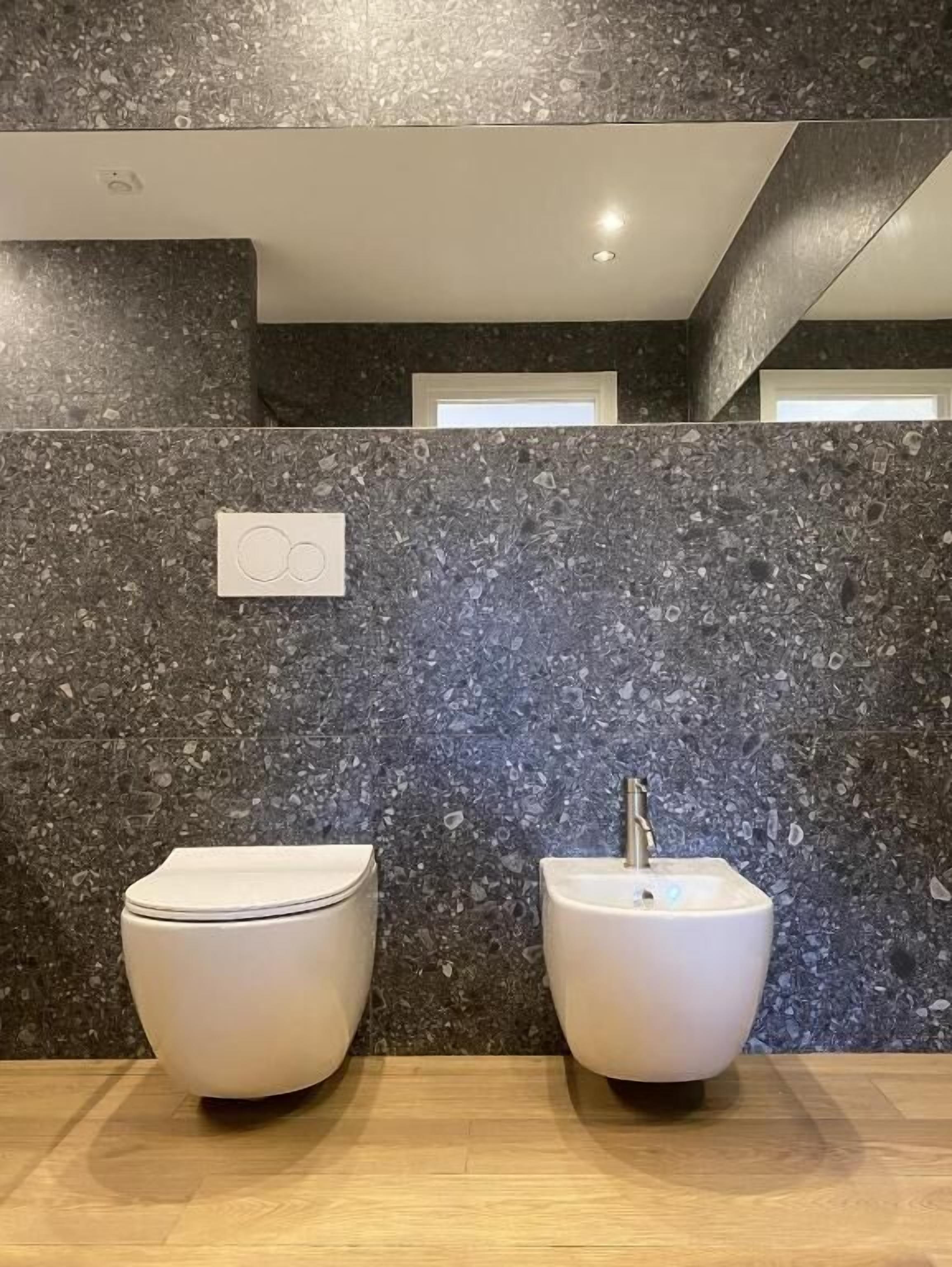 Um banheiro moderno com painel de granito, vaso sanitário e bidê.