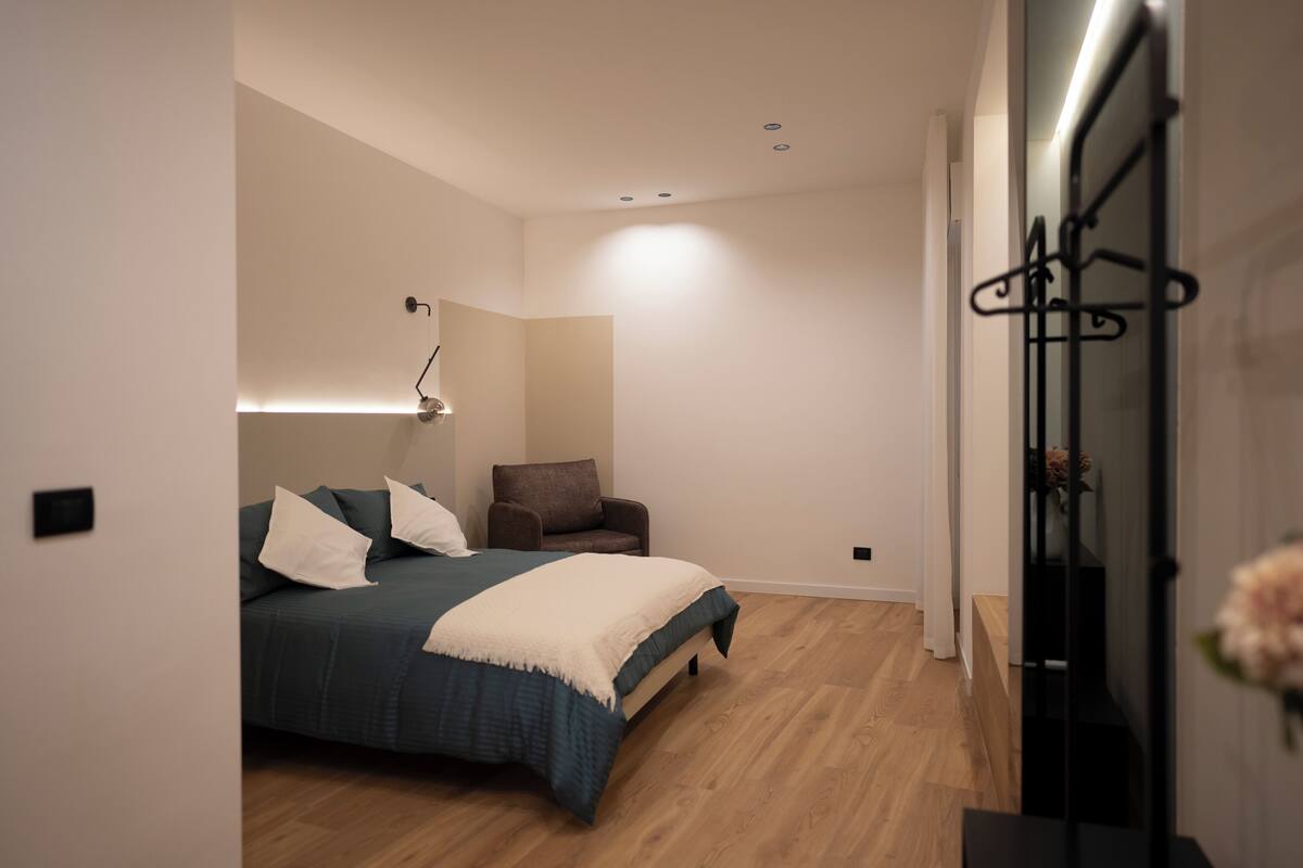 Une chambre à coucher comprenant un lit, une chaise, une table de chevet et une lampe fixée au mur.