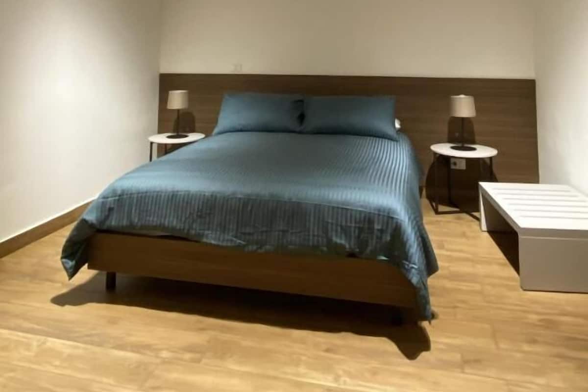 Une chambre moderne avec un lit en bois, deux tables de chevet avec des lampes, un luminaire au plafond et un appareil de climatisation.