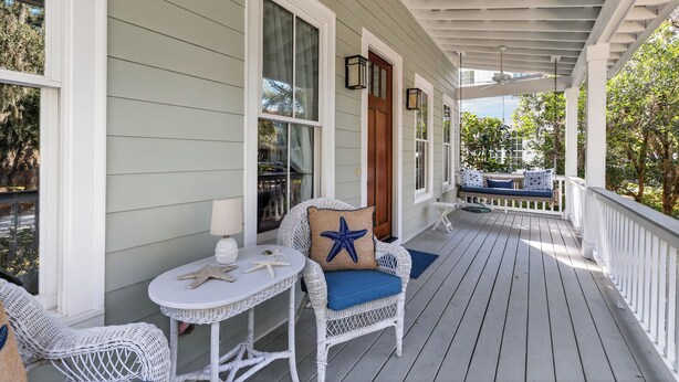 Een overdekte veranda met witte rieten meubels, een ronde tafel en een houten deur.