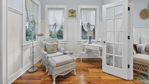 Een kamer met een witte rotan stoel, een bureau en een bed.